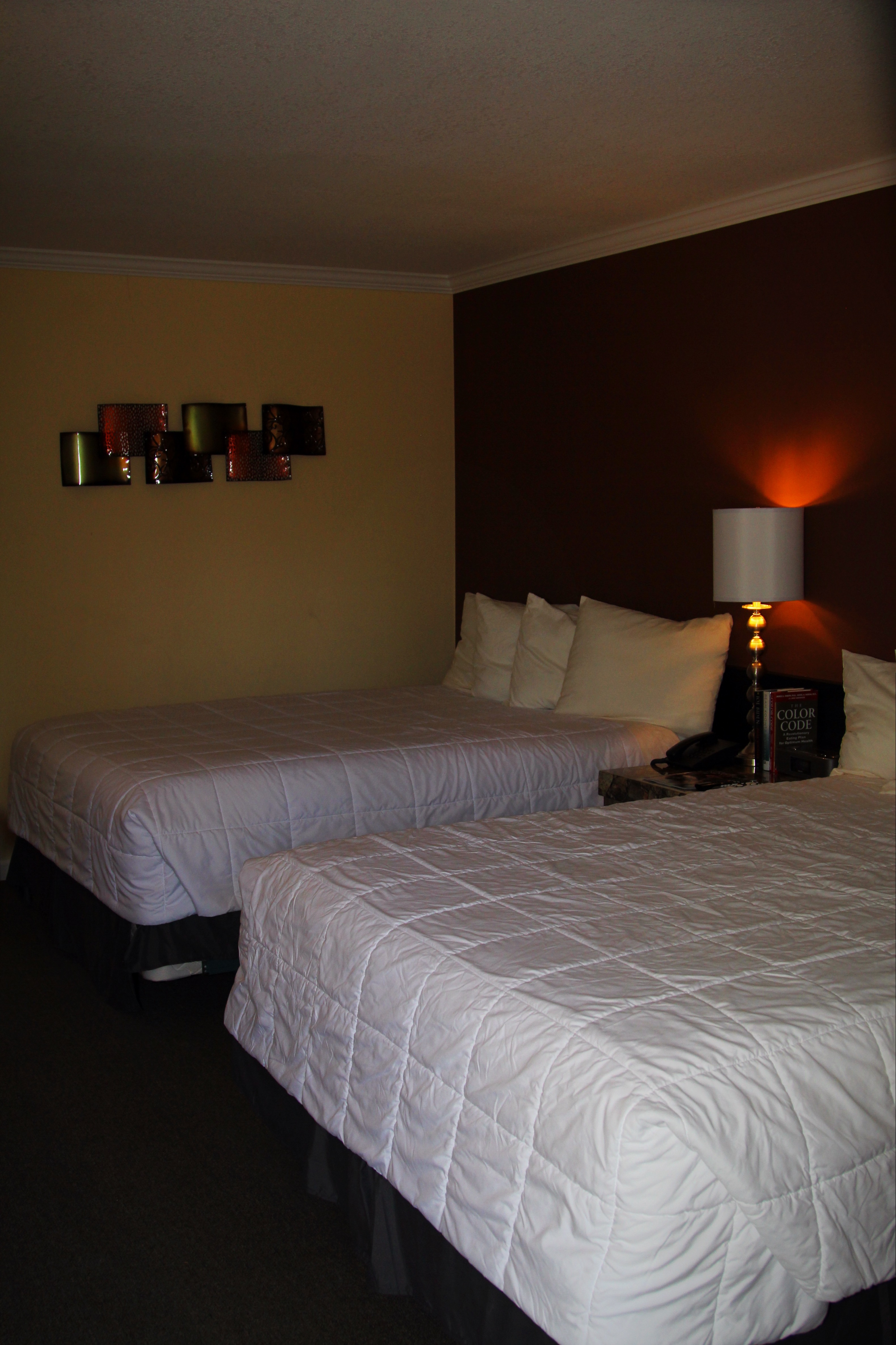 A hotel room with two beds, a nightstand with a lamp, and artwork on the wall.